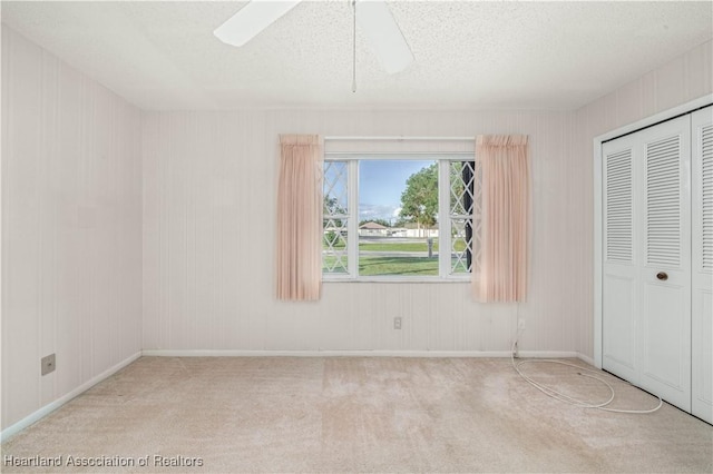 unfurnished bedroom featuring ceiling fan, light colored carpet, a textured ceiling, and a closet