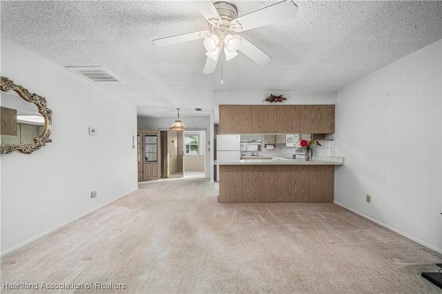 kitchen with decorative light fixtures, white appliances, kitchen peninsula, light carpet, and a textured ceiling