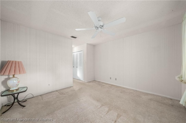 empty room with light carpet, ceiling fan, and a textured ceiling