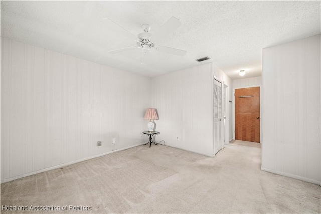 unfurnished room featuring ceiling fan, light carpet, and a textured ceiling