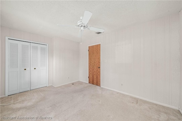 unfurnished bedroom featuring light carpet, ceiling fan, a closet, and a textured ceiling