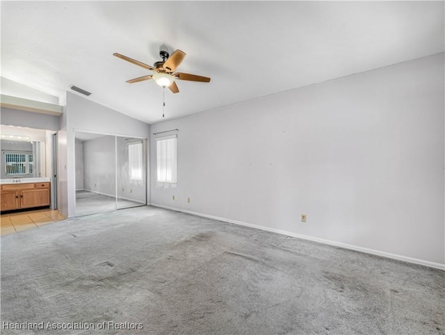 unfurnished bedroom featuring ceiling fan, connected bathroom, vaulted ceiling, light colored carpet, and a closet