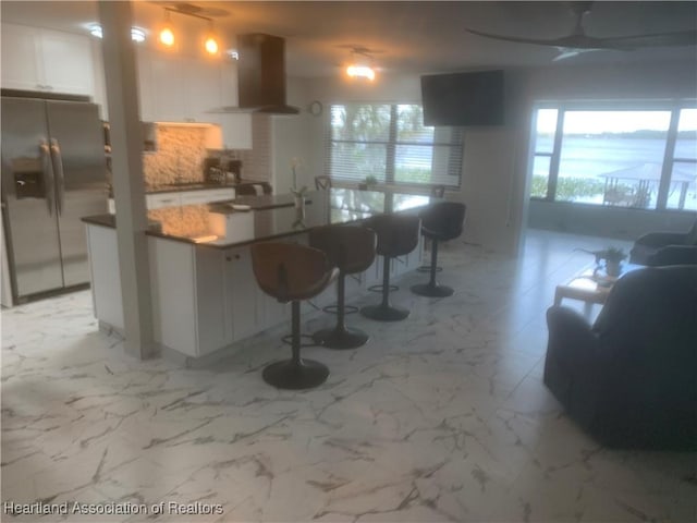 kitchen with marble finish floor, stainless steel fridge, white cabinetry, and range hood