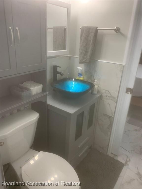 bathroom featuring marble finish floor, vanity, toilet, and tile walls