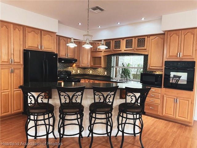 5717 Longbow Dr, Sebring, FL 33876 - kitchen with black appliances, under cabinet range hood, tasteful backsplash, a kitchen bar, and dark countertops