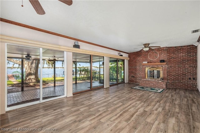 unfurnished living room with a water view, hardwood / wood-style flooring, ornamental molding, a fireplace, and brick wall