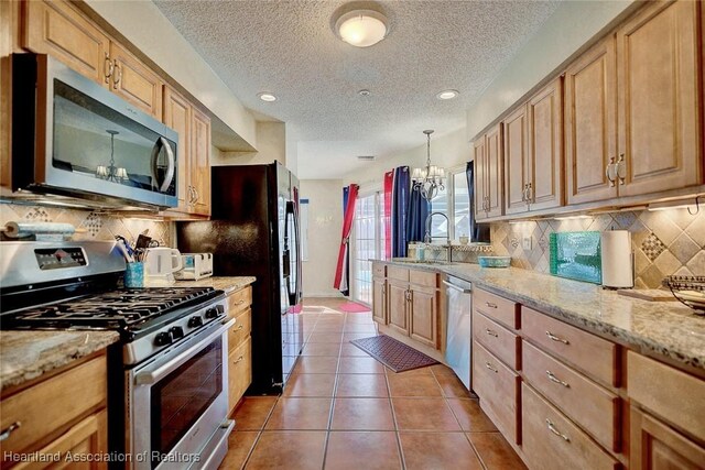 kitchen featuring sink, hanging light fixtures, stainless steel appliances, light stone counters, and light tile patterned flooring