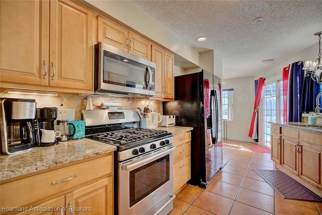 kitchen with hanging light fixtures, light tile patterned floors, a textured ceiling, light brown cabinetry, and stainless steel appliances