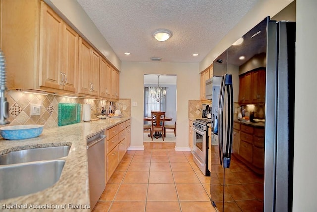 kitchen featuring stainless steel appliances, pendant lighting, a textured ceiling, light brown cabinetry, and light tile patterned flooring