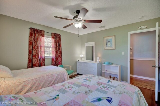 bedroom with ceiling fan, wood-type flooring, and a textured ceiling