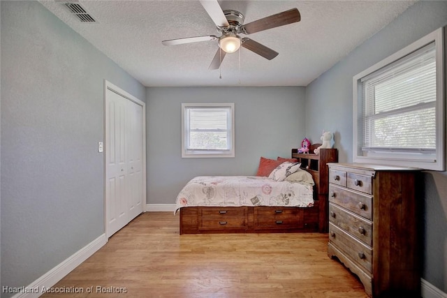 bedroom featuring ceiling fan, light wood-type flooring, a closet, and a textured ceiling