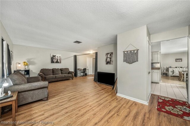 living area with light wood-type flooring, visible vents, and a textured ceiling