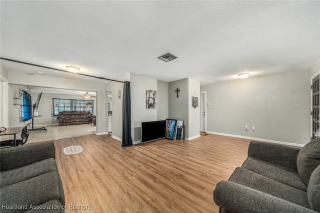 living room featuring light wood finished floors, baseboards, visible vents, and a textured ceiling