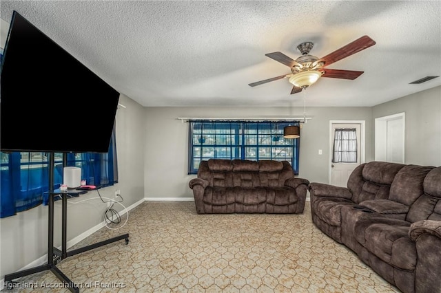 living area featuring a ceiling fan, visible vents, a textured ceiling, and baseboards