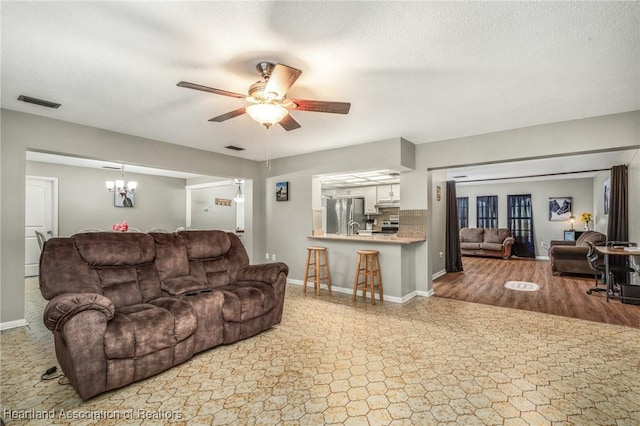 living area with visible vents, a textured ceiling, baseboards, and ceiling fan with notable chandelier