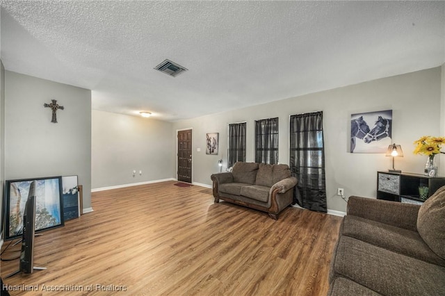 living room with light wood finished floors, baseboards, visible vents, and a textured ceiling