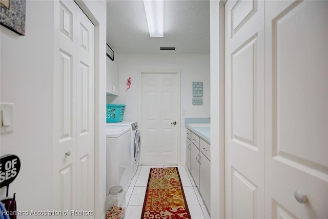 laundry room with light tile patterned floors, washer and clothes dryer, cabinets, and a textured ceiling