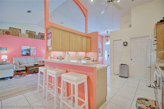 kitchen featuring a breakfast bar area, high vaulted ceiling, light tile patterned floors, light brown cabinets, and ceiling fan