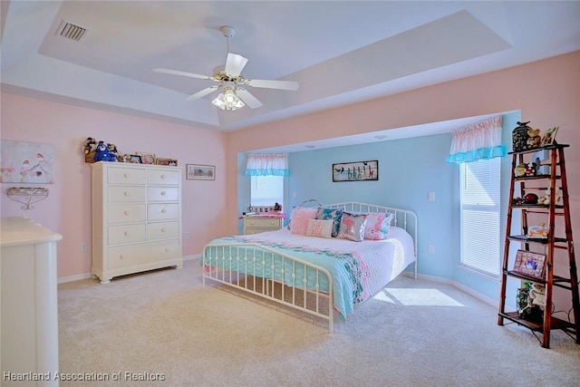 bedroom featuring a raised ceiling, light colored carpet, and multiple windows