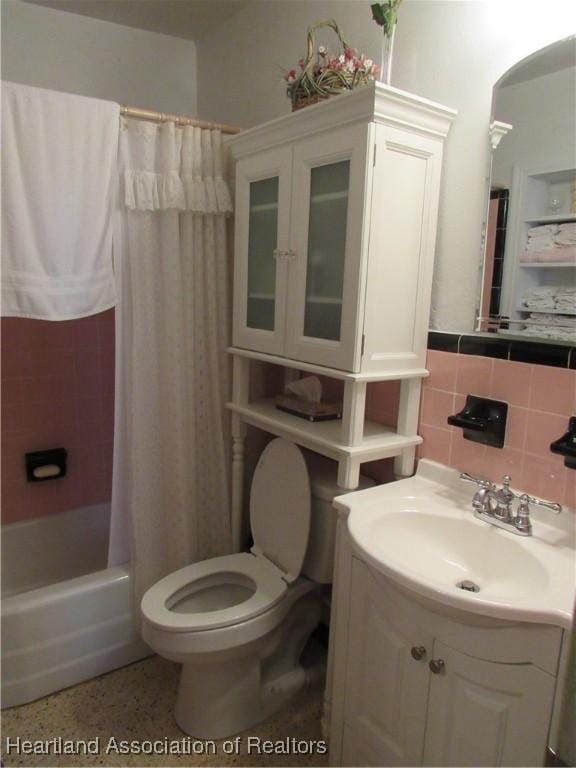 bathroom with vanity, toilet, shower / bath combo with shower curtain, speckled floor, and backsplash