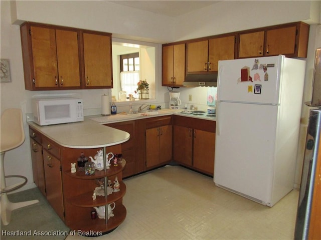 kitchen featuring white appliances, light countertops, under cabinet range hood, brown cabinets, and a sink