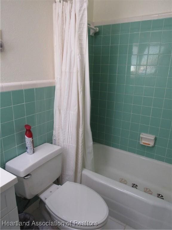bathroom featuring wainscoting, vanity, toilet, shower / bathtub combination with curtain, and tile walls