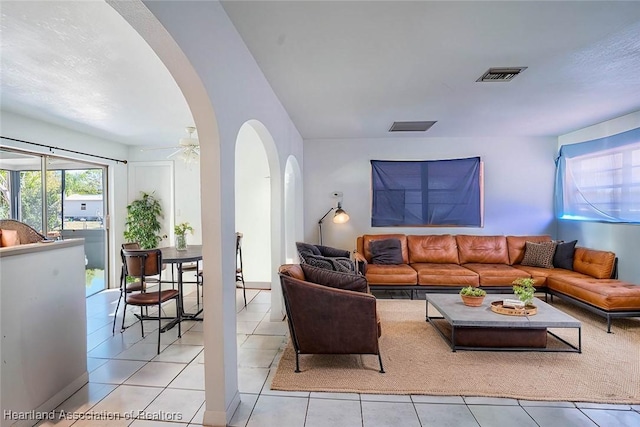 living room featuring arched walkways, light tile patterned floors, visible vents, and a ceiling fan