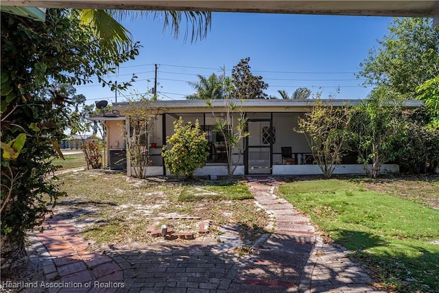 view of front of property with central air condition unit, a sunroom, and a front lawn