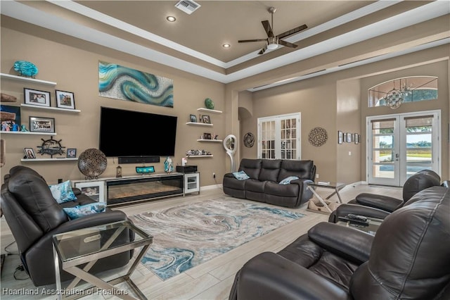 living room with a raised ceiling, ornamental molding, french doors, and ceiling fan