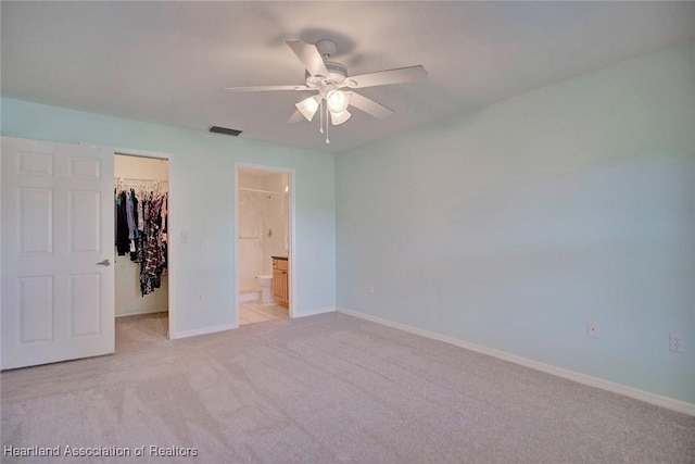 unfurnished bedroom featuring ceiling fan, ensuite bathroom, light colored carpet, a walk in closet, and a closet