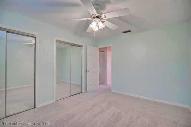 unfurnished bedroom featuring ceiling fan, light carpet, and two closets