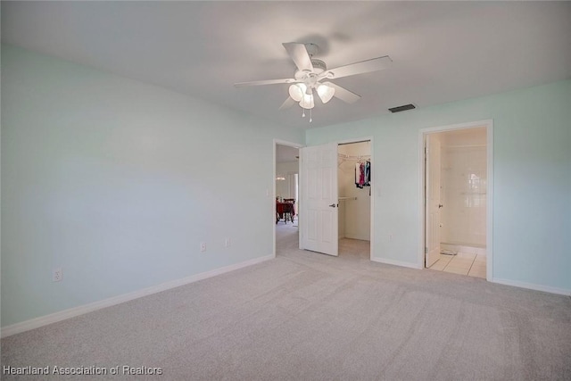 unfurnished bedroom with light carpet, ensuite bathroom, a walk in closet, ceiling fan, and a closet