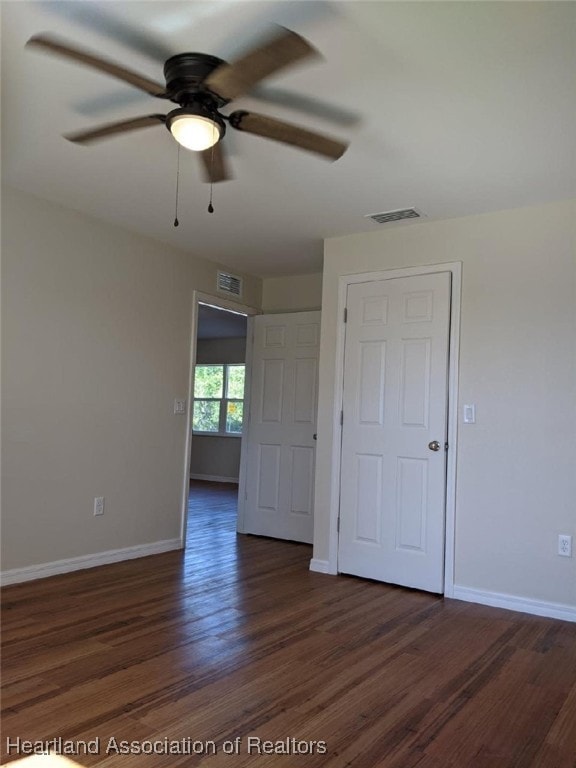 empty room featuring baseboards, visible vents, a ceiling fan, and dark wood-style floors