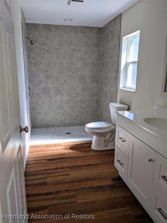 bathroom featuring toilet, wood finished floors, vanity, and a tile shower