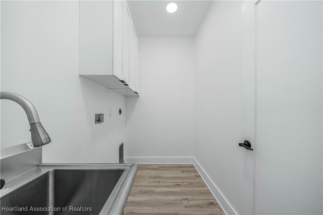 laundry area featuring sink, light hardwood / wood-style flooring, and cabinets