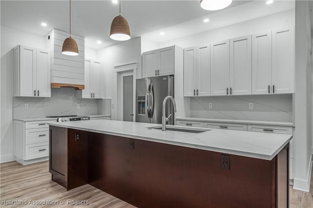 kitchen featuring pendant lighting, white cabinetry, an island with sink, sink, and stainless steel fridge with ice dispenser