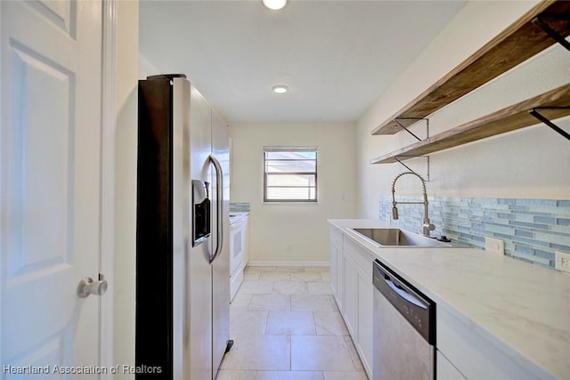 kitchen featuring sink, white cabinetry, appliances with stainless steel finishes, light stone countertops, and backsplash