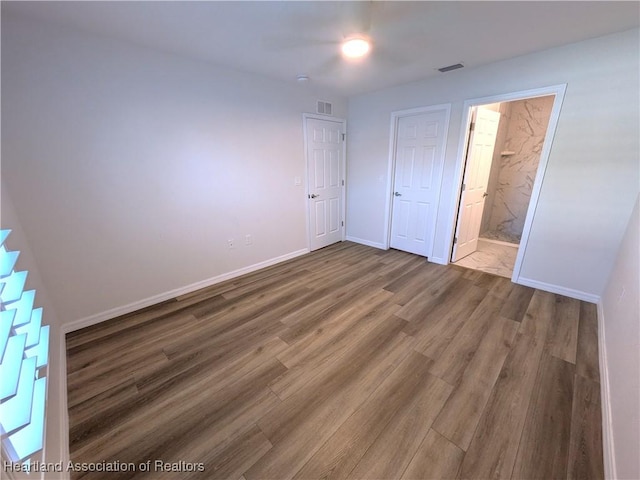 unfurnished bedroom with a closet, ensuite bath, and wood-type flooring