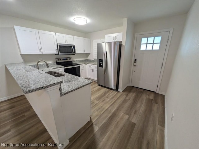 kitchen featuring sink, white cabinetry, hardwood / wood-style floors, kitchen peninsula, and appliances with stainless steel finishes