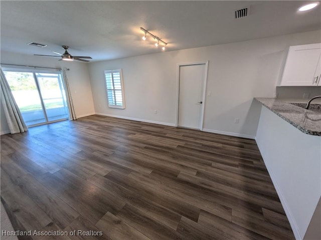 unfurnished living room with dark wood-type flooring, rail lighting, ceiling fan, and sink