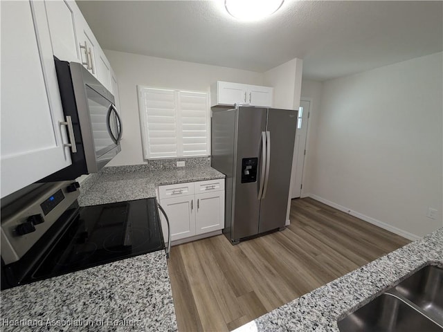 kitchen featuring appliances with stainless steel finishes, light hardwood / wood-style floors, white cabinets, and light stone counters