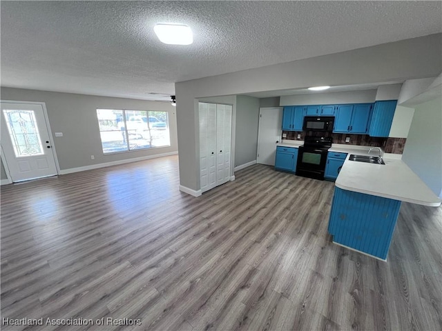 kitchen with a breakfast bar, sink, blue cabinetry, black appliances, and kitchen peninsula