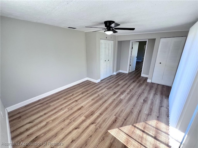 unfurnished bedroom featuring a textured ceiling, ceiling fan, light hardwood / wood-style floors, and multiple closets