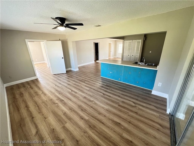 unfurnished living room featuring a textured ceiling, hardwood / wood-style flooring, sink, and ceiling fan