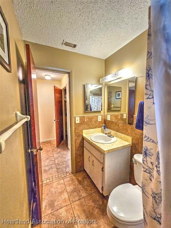 bathroom featuring tile patterned floors, a textured ceiling, toilet, vanity, and tile walls