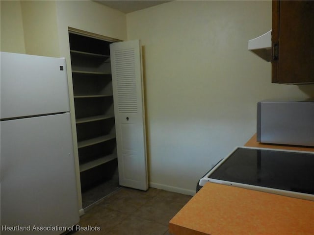 kitchen featuring dark brown cabinetry, stove, white fridge, and tile patterned flooring