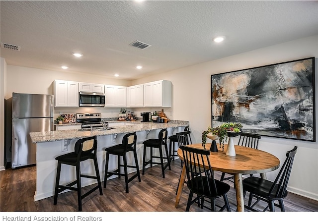 kitchen with light stone countertops, dark hardwood / wood-style flooring, stainless steel appliances, and white cabinetry