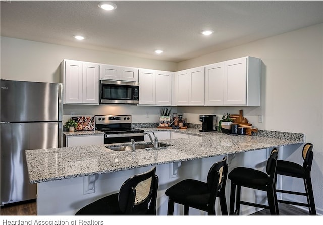 kitchen featuring light stone countertops, white cabinetry, sink, stainless steel appliances, and kitchen peninsula