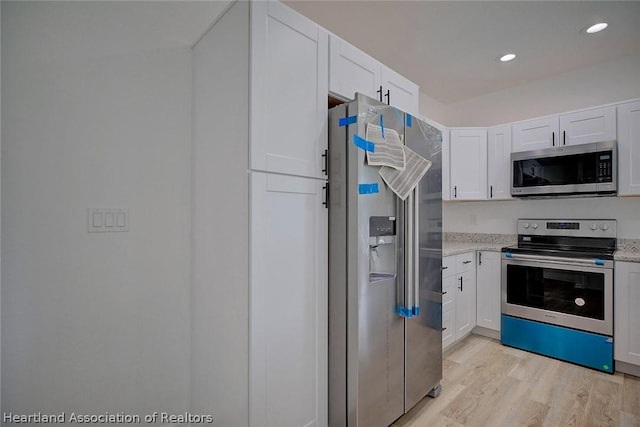 kitchen with white cabinetry, stainless steel appliances, light stone counters, and light wood-type flooring