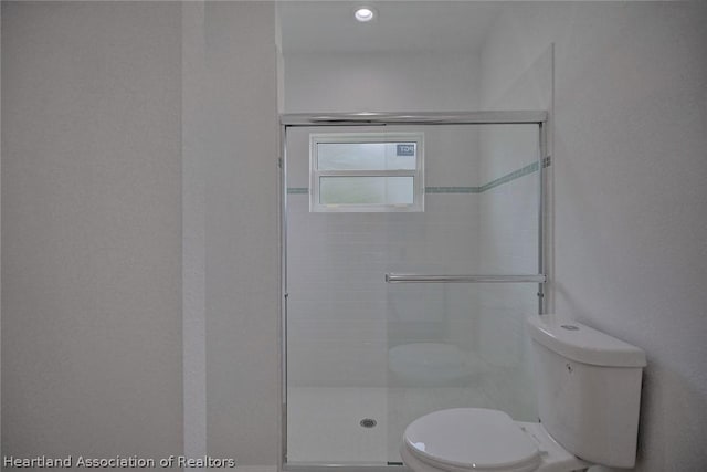 bathroom featuring toilet and a shower with shower door